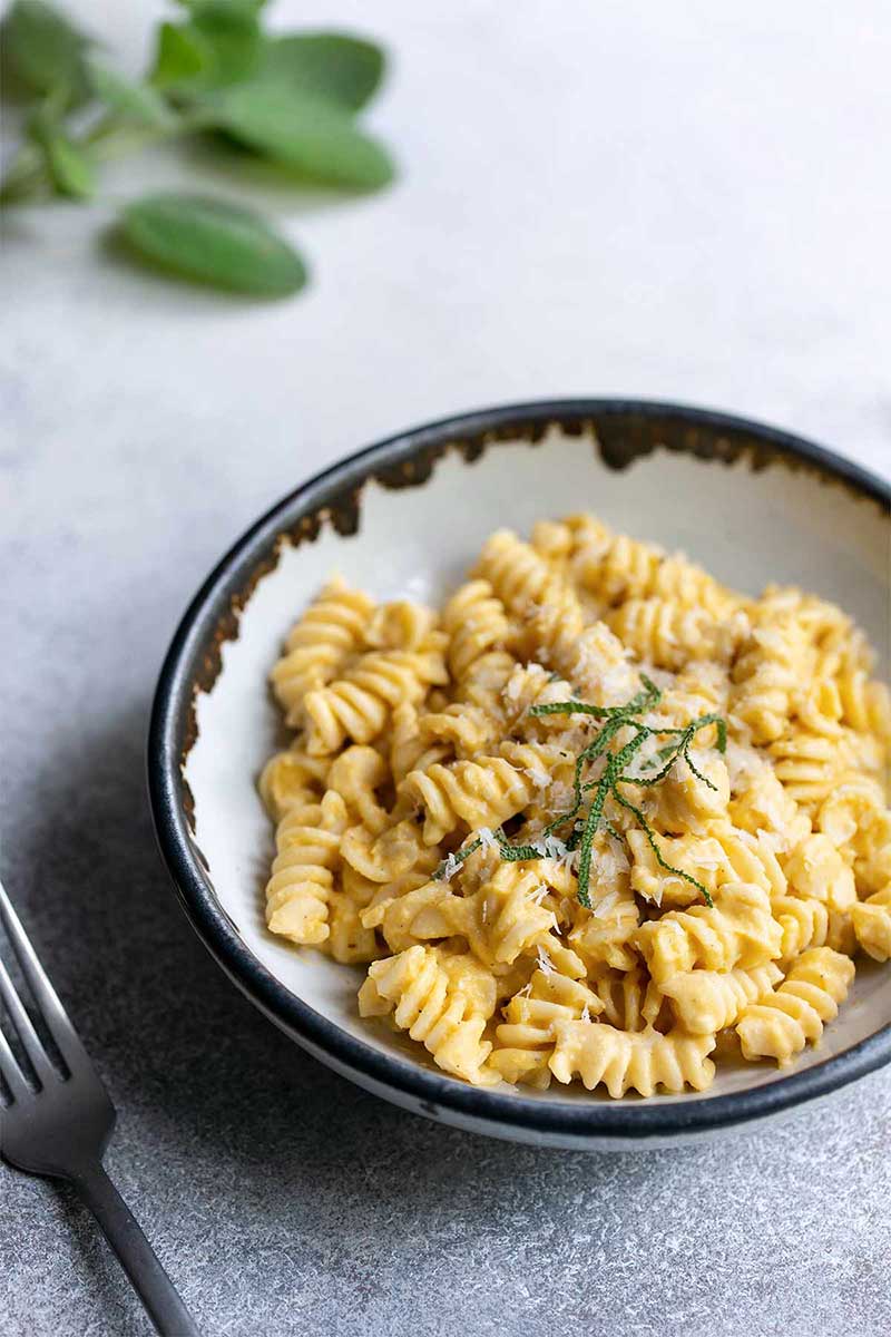 Side angle view of butternut squash pasta recipe topped with sage and grated parmesan cheese