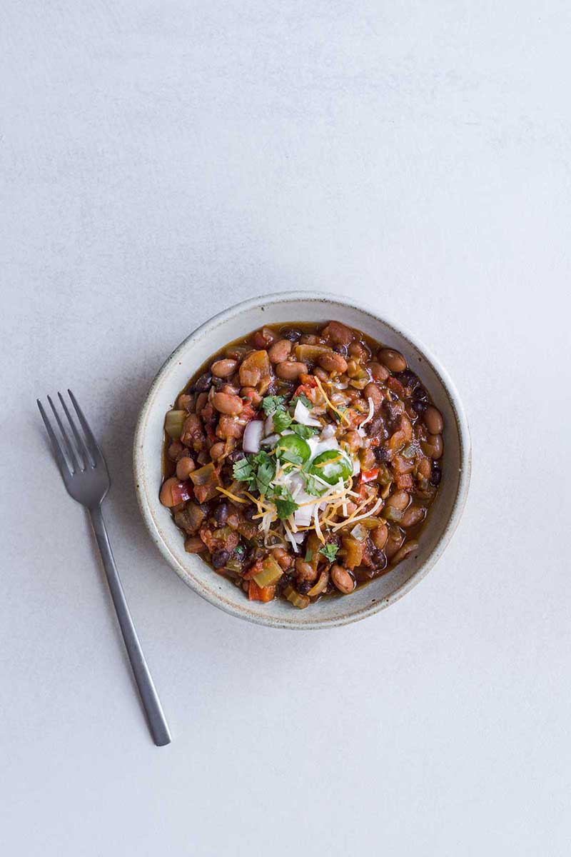Vegetarian chili in a bowl, topped with sour cream, cheese, and sliced jalapeños