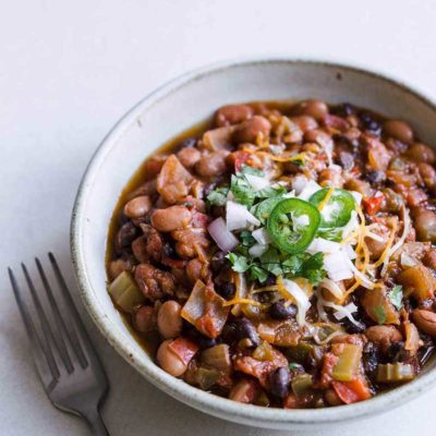 Closeup of vegan chili in white bowl topped with topped with sour cream. hot peppers and cheese