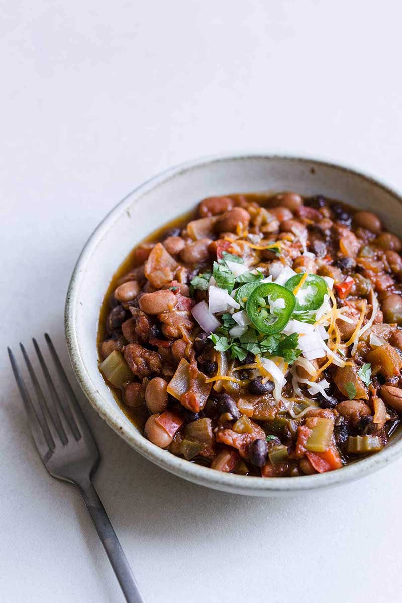 Closeup of vegan chili in white bowl topped with topped with sour cream. hot peppers and cheese