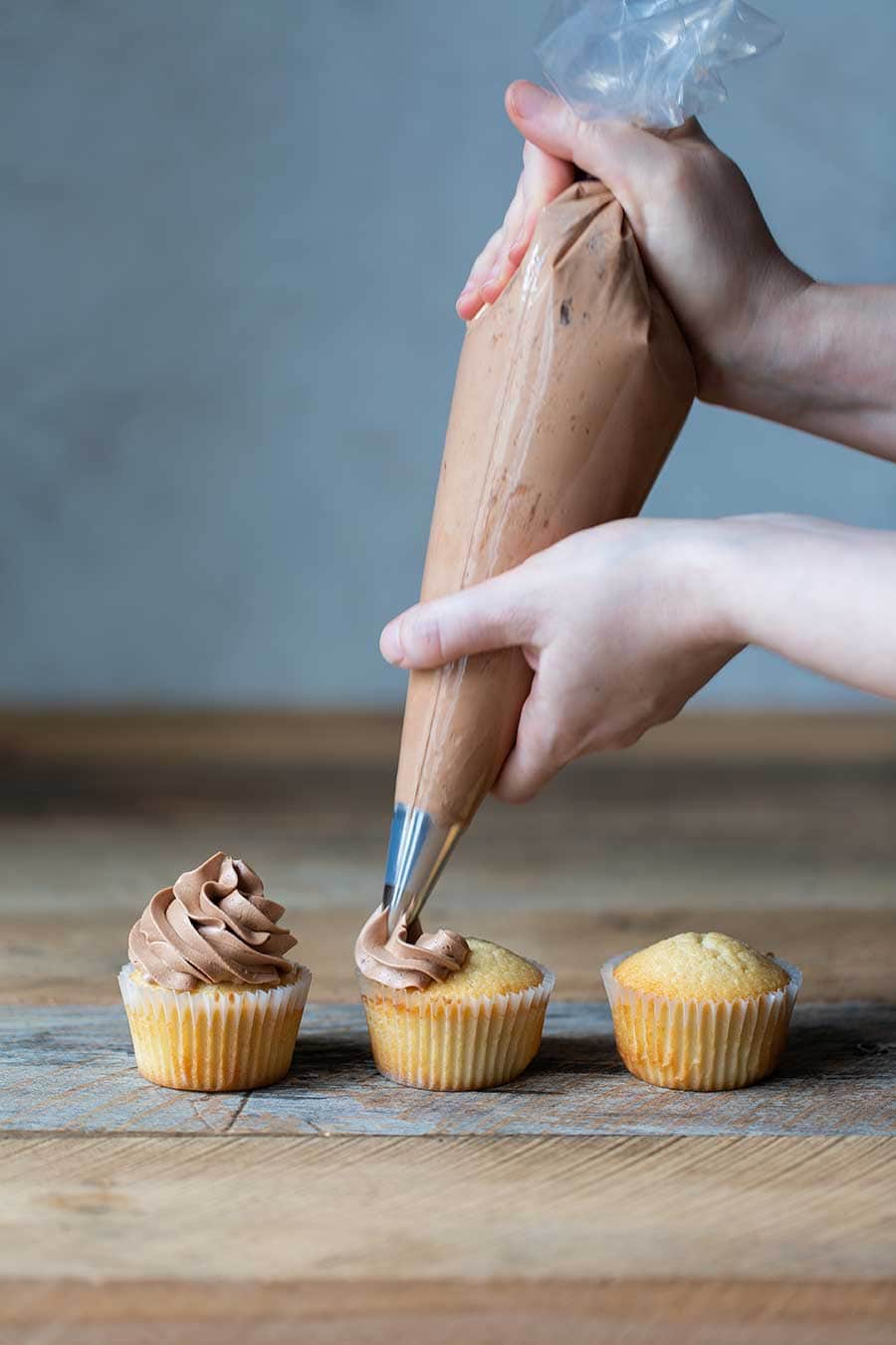 Piping chocolate frosting onto vanilla cupcakes