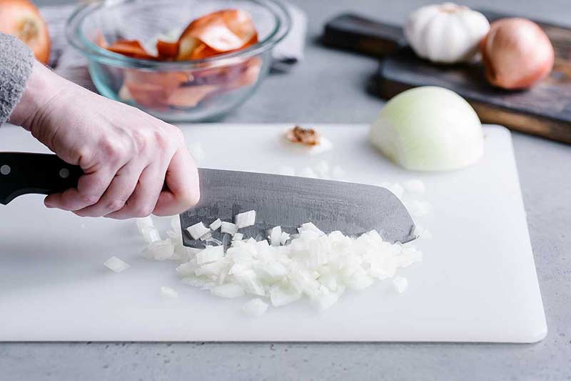Running a knife through chopped onions on a cutting board