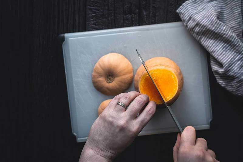 demonstrating how to use a knife to slice the squash down the center, lengthwise