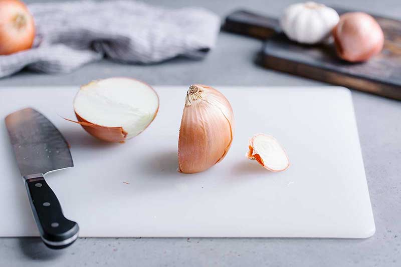 Two onion halves on a cutting board with a chef's knife