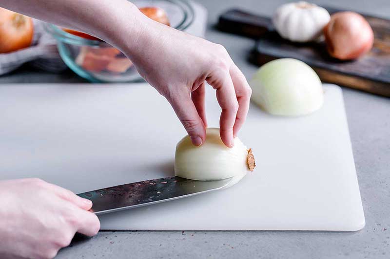 Using a knife to slice an onion half correctly