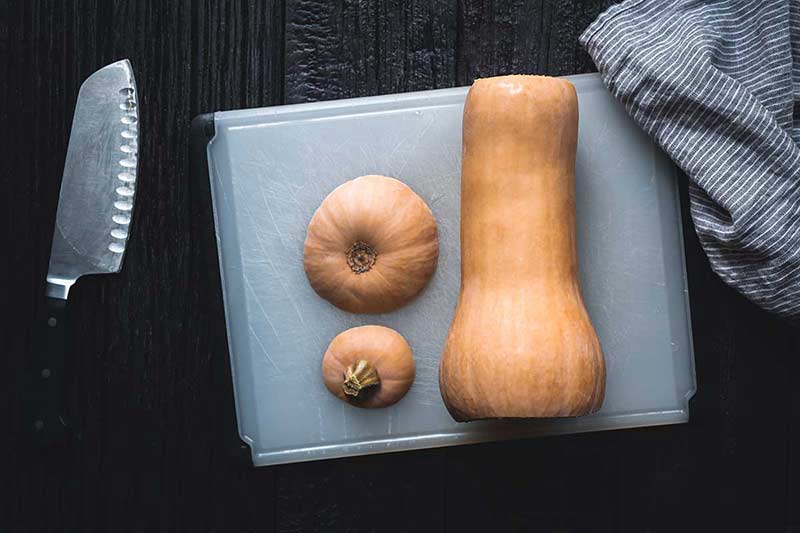 a cutting board and knife, as well as squash that has had the top and bottom sliced off