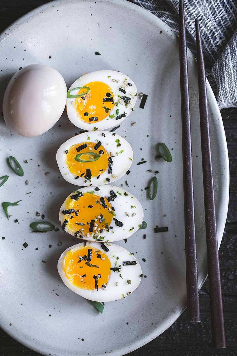 Ramen eggs close up on a plate with garnishes and chopsticks