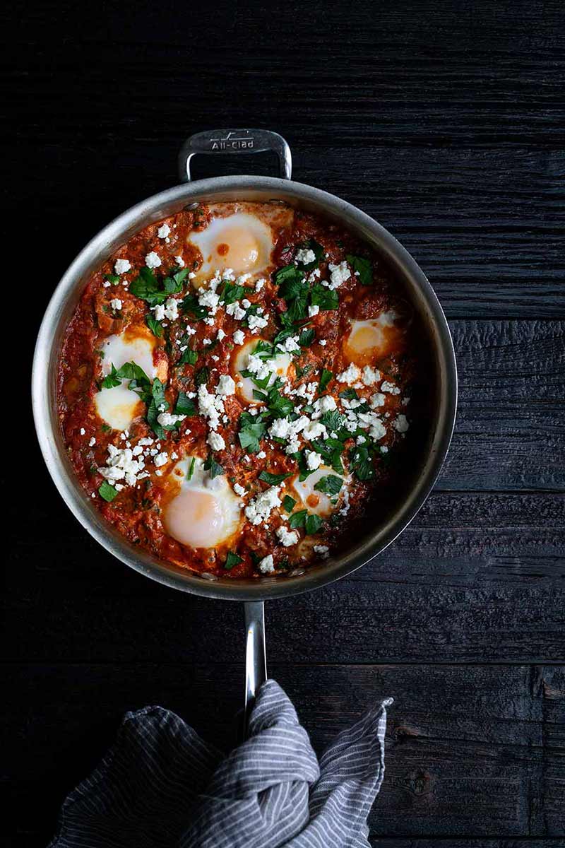 Shakshuka recipe in a skillet with a towel around handle of pan
