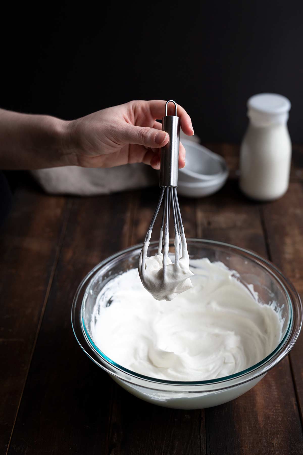 A hand holding a whisk over a bowl of whipped cream