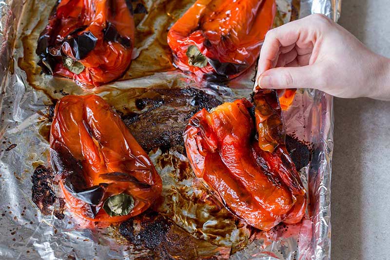 A hand peeling roasted red peppers