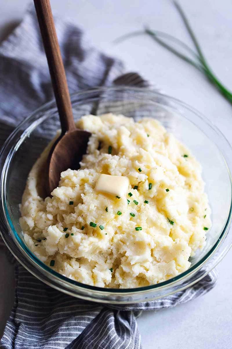 cheesy mashed potatoes in a bowl topped with chives and butter