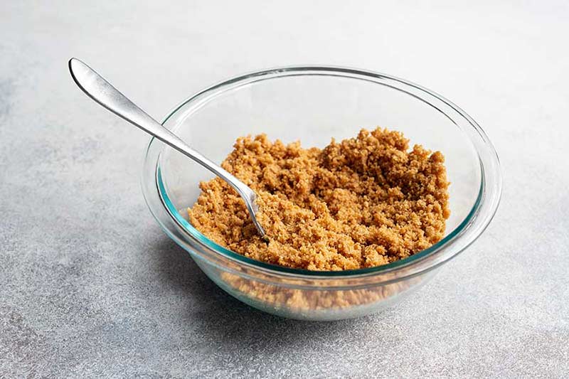 Graham cracker crumbs and melted butter stirred together in a bowl with a fork