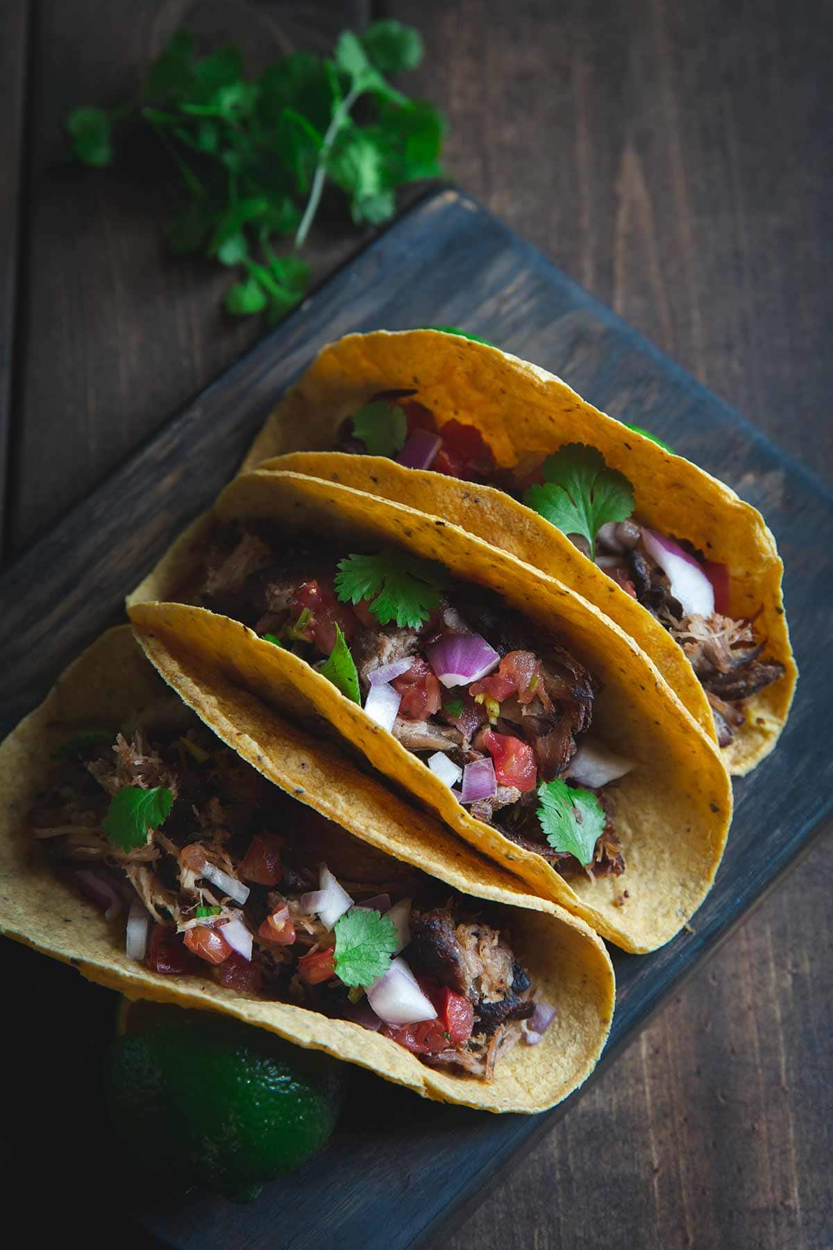 Three pork carnitas tacos lined up on a cutting board