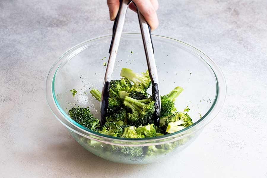 tossing broccoli in a bowl with tongs