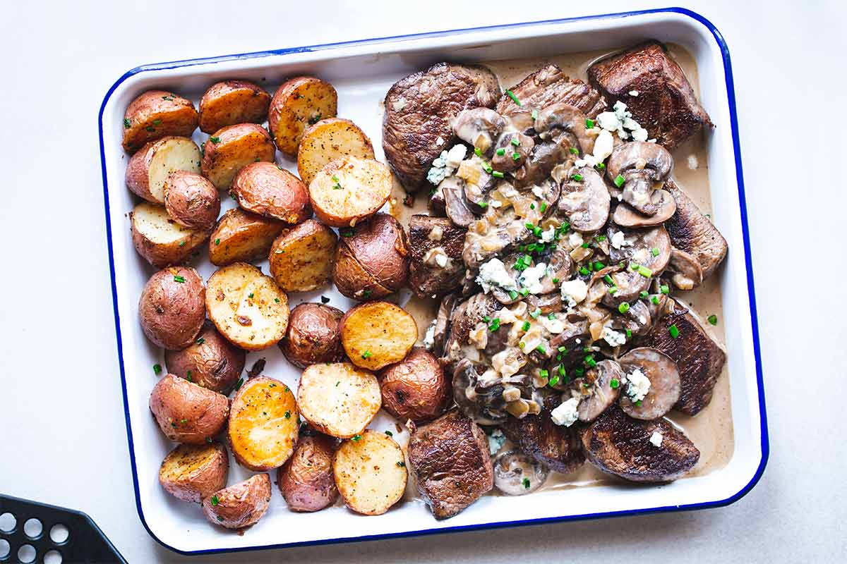 Steak tips recipe with mushrooms, blue cheese sauce and potatoes on a sheet pan, shot from overhead