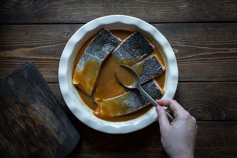 spooning marinade over the uncooked salmon