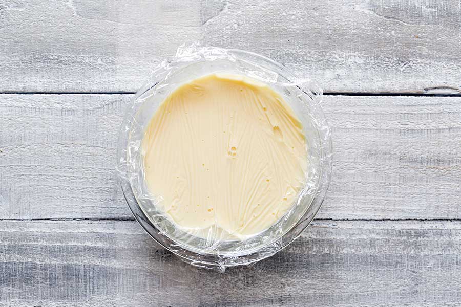Pressing plastic film against the lemon ice cream base to prevent a skin from forming