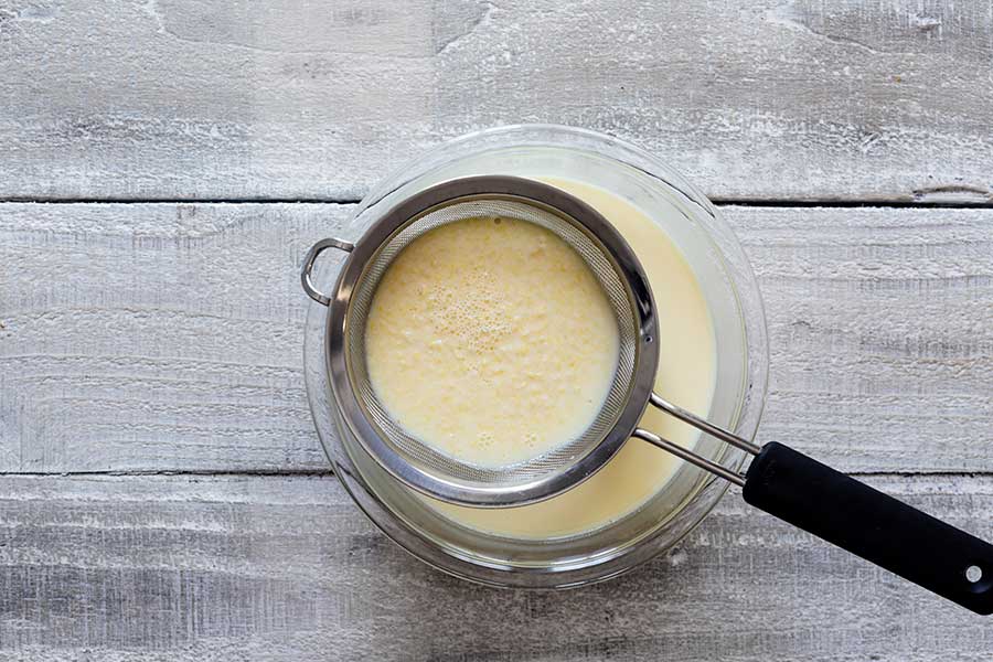 Straining lemon zest out of the ice cream base using a fine mesh strainer set over a bowl