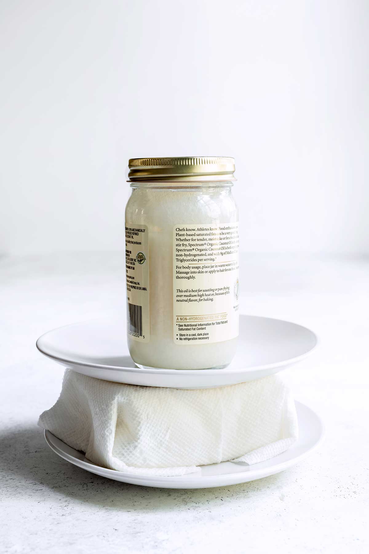 Pressing tofu between two plates using paper towels. A jar of coconut oil is sitting on top for weight.