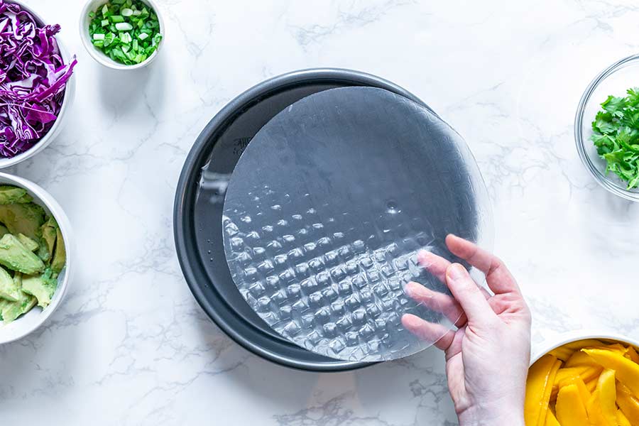 A rice paper wrapper being dipped into a cake pan full of water