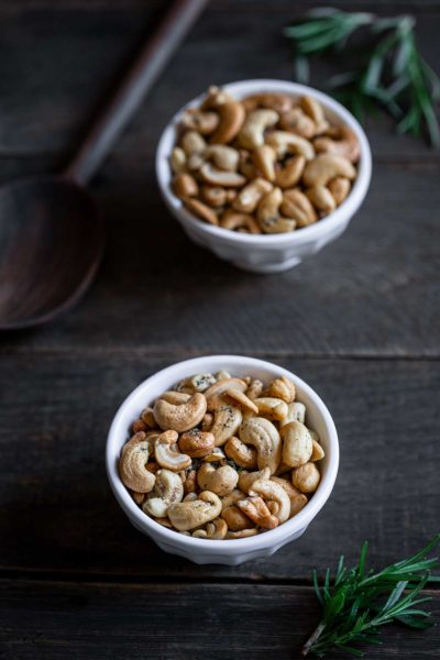Rosemary salt and pepper cashews in two white bowls next to a wooden spoon
