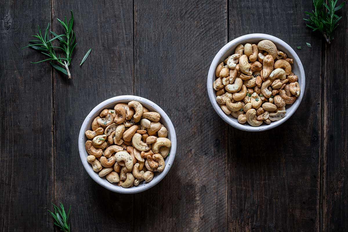 Rosemary salt and pepper cashews in two white bowls next to fresh rosemary