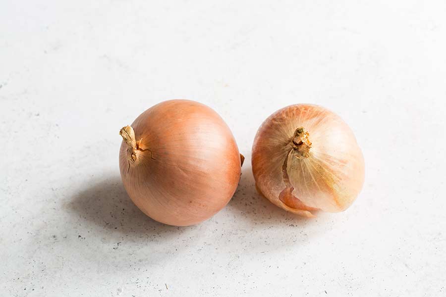 Two yellow onions on a white surface