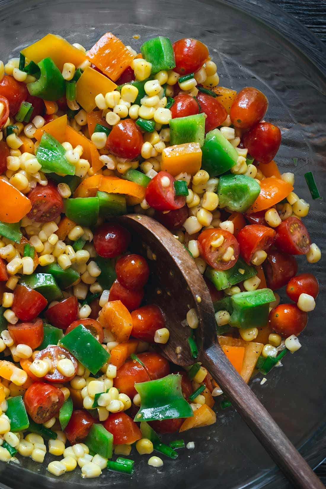 Corn salad in a grey bowl surrounded by bell peppers and tomatoes
