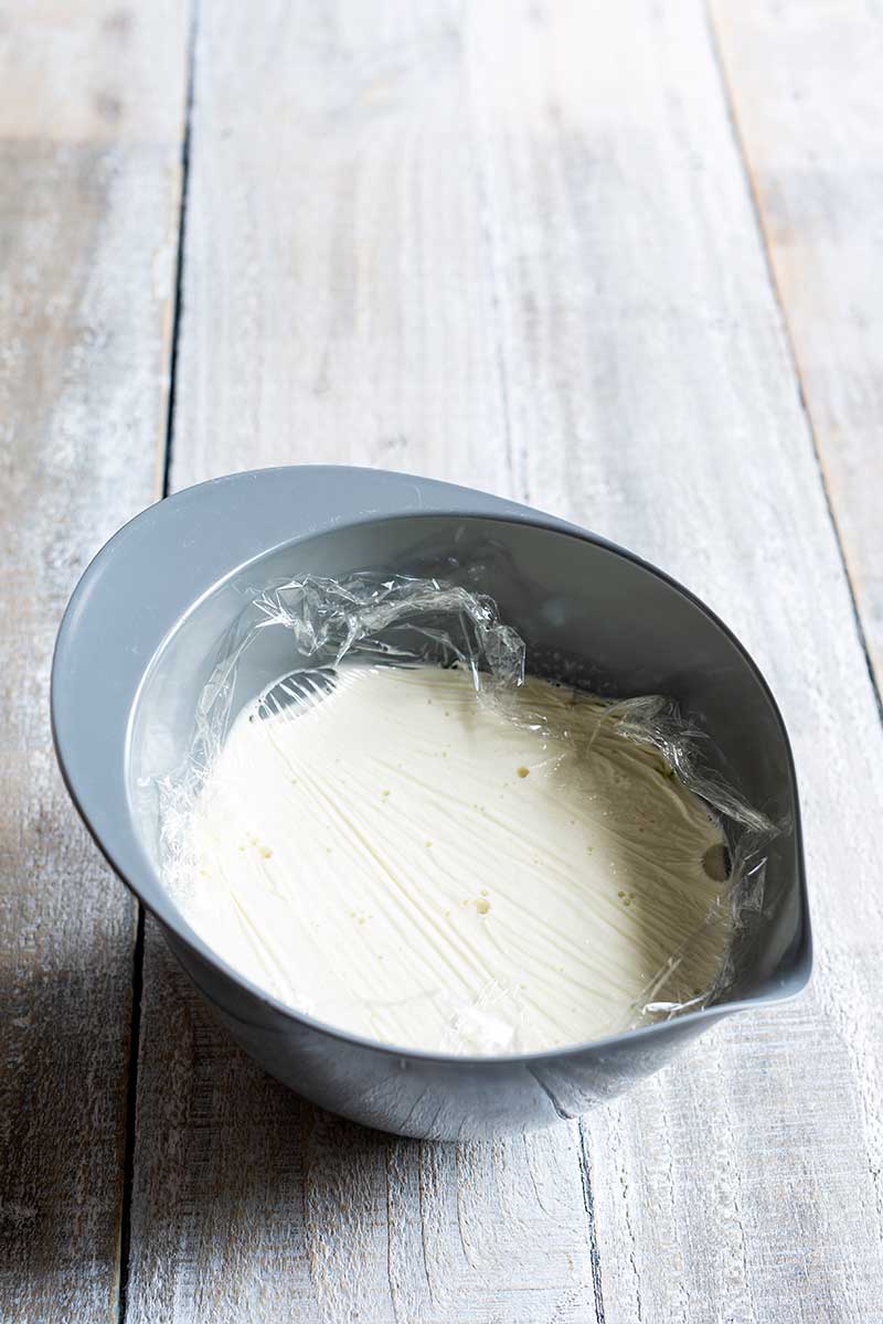 Olive oil ice cream base in a bowl covered with plastic wrap pressed directly against surface