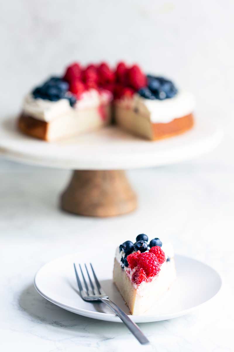 A slice of berry cake on a plate with a fork in front of the remaining cake