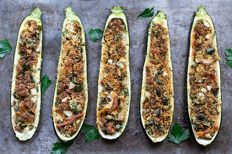 Finished stuffed zucchini on a sheet pan surrounded by fresh parsley