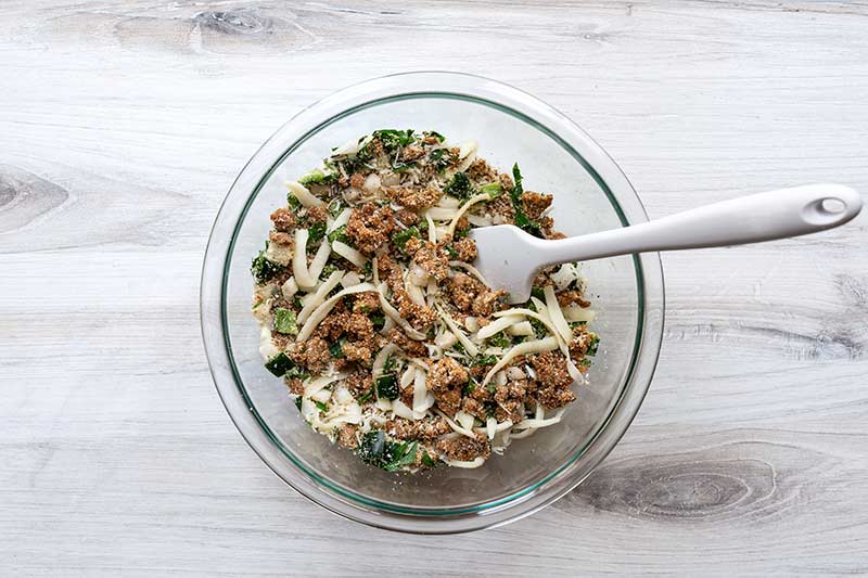 A bowl with zucchini boat filling and a spatula