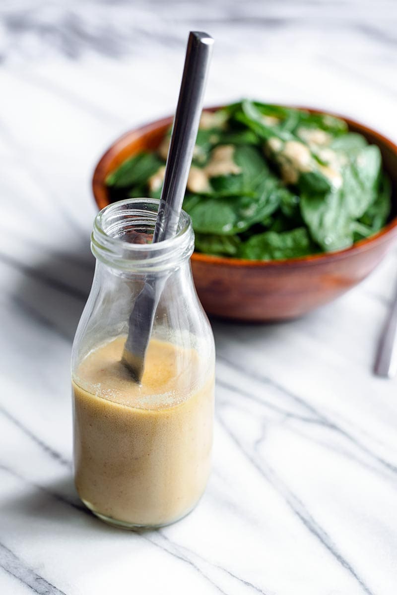 Tahini dressing in a jar with a butter knife in the jar for stirring, with salad in the background
