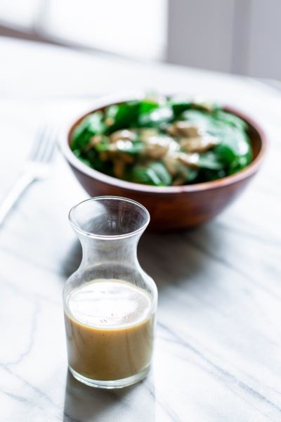 Finished tahini dressing recipe in a glass bottle with salad in the background
