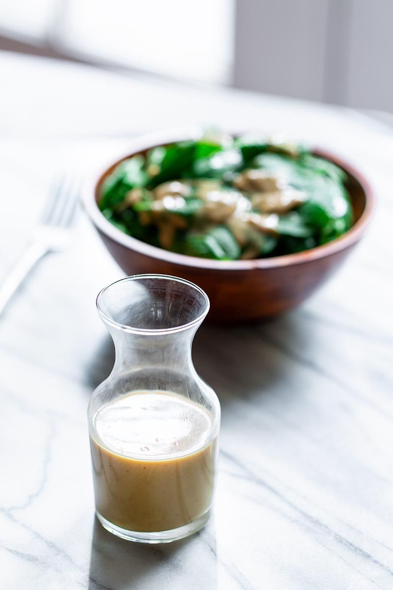 Finished tahini dressing recipe in a glass bottle with salad in the background