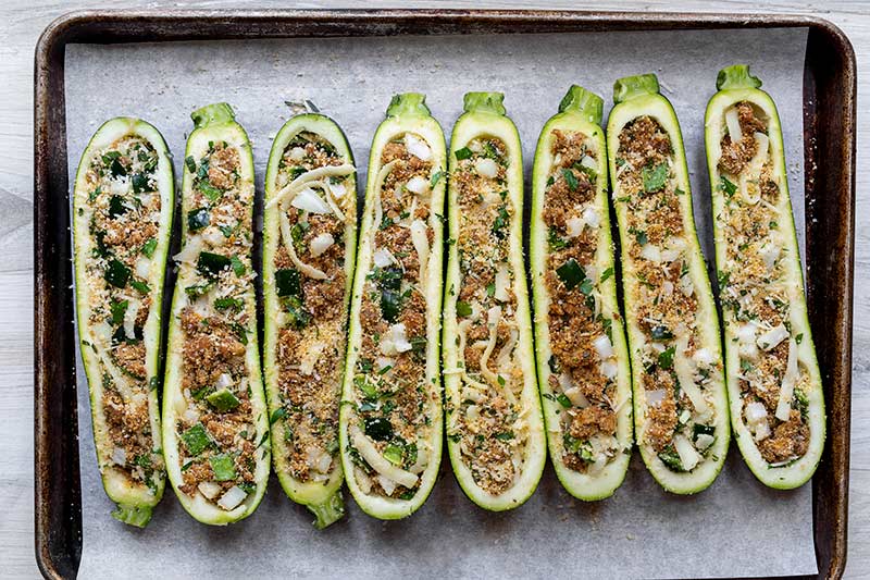 uncooked stuffed zucchini on a parchment lined sheet pan