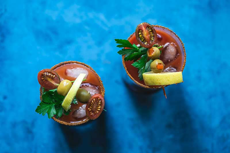 overhead photo: Two V8 Bloody Mary cocktails on a blue backdrop