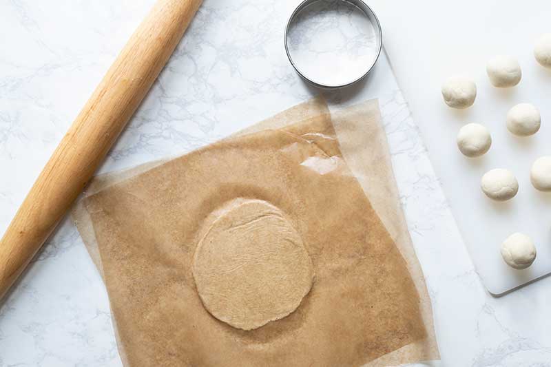 Dough between two pieces of wax paper next to a rolling pin and biscuit butter