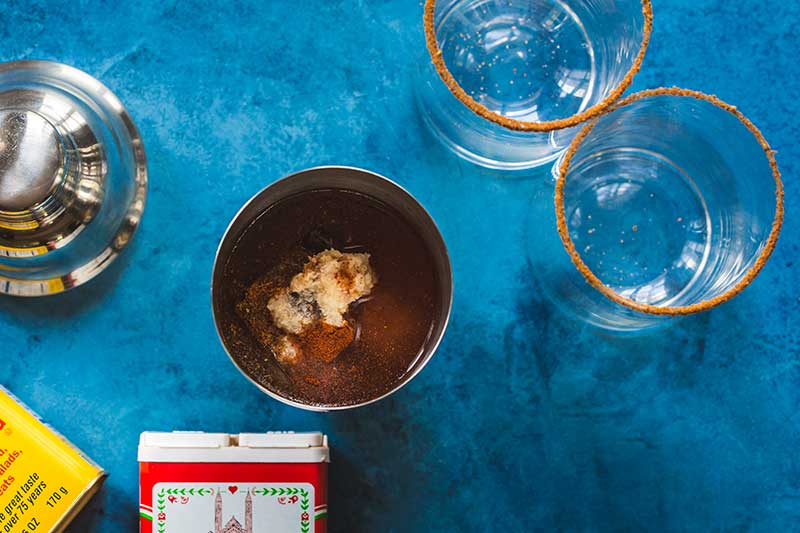 Overhead shot of two Old Bay rimmed highball glasses, spice containers, and a cocktail shaker full of bloody Mary ingredients