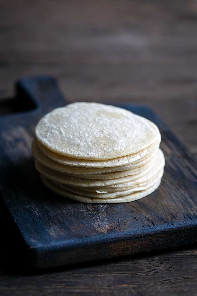 A stack of homemade corn tortillas on a cutting board