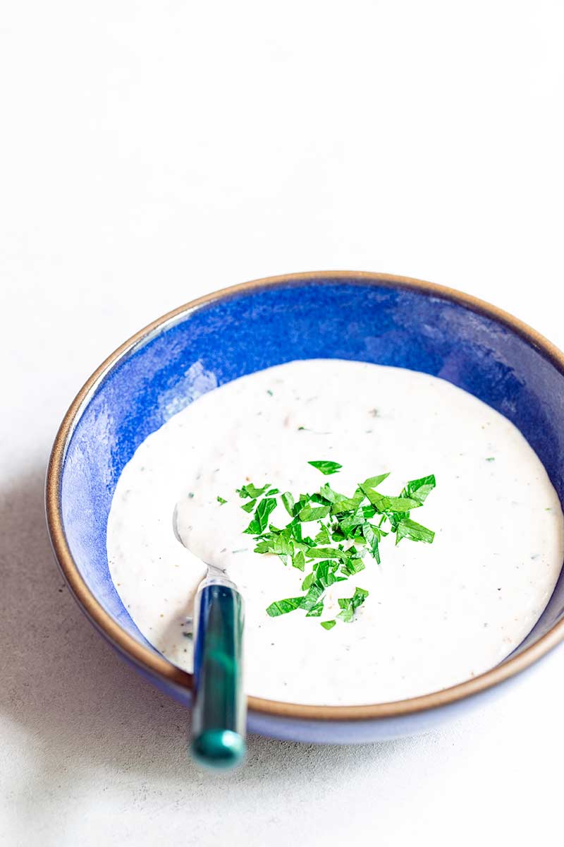 serving spoon in a blue bowl filled with a creamy white condiment topped with chopped parsley
