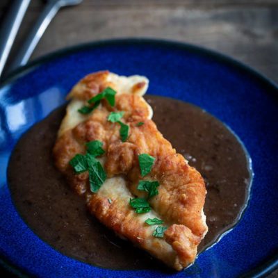 A photo of pan-seared chicken breast topped with a pan sauce recipe and fresh chopped parsley