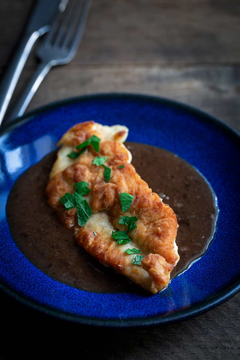 A photo of pan-seared chicken breast topped with a pan sauce and fresh chopped parsley