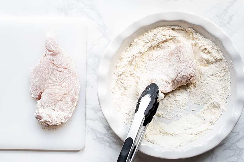 Dredged chicken being pan seared in a stainless steel skillet
