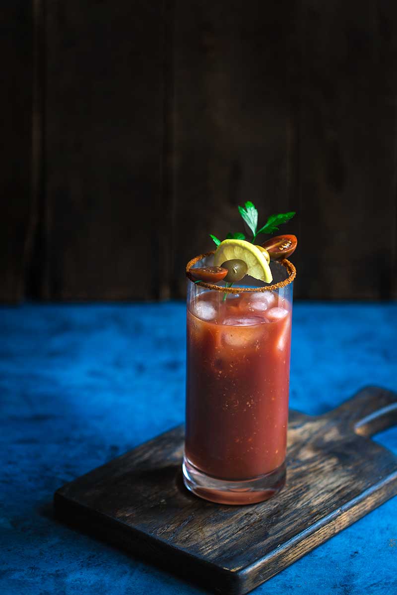 Old Bay Bloody Mary Recipe topped with garnishes on a blue backdrop