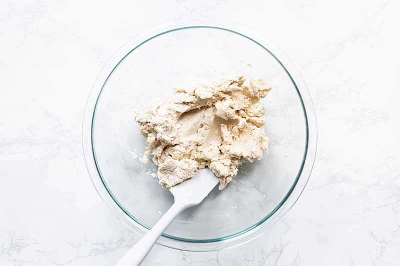 Gritty, just-stirred masa and water with a spatula in a bowl