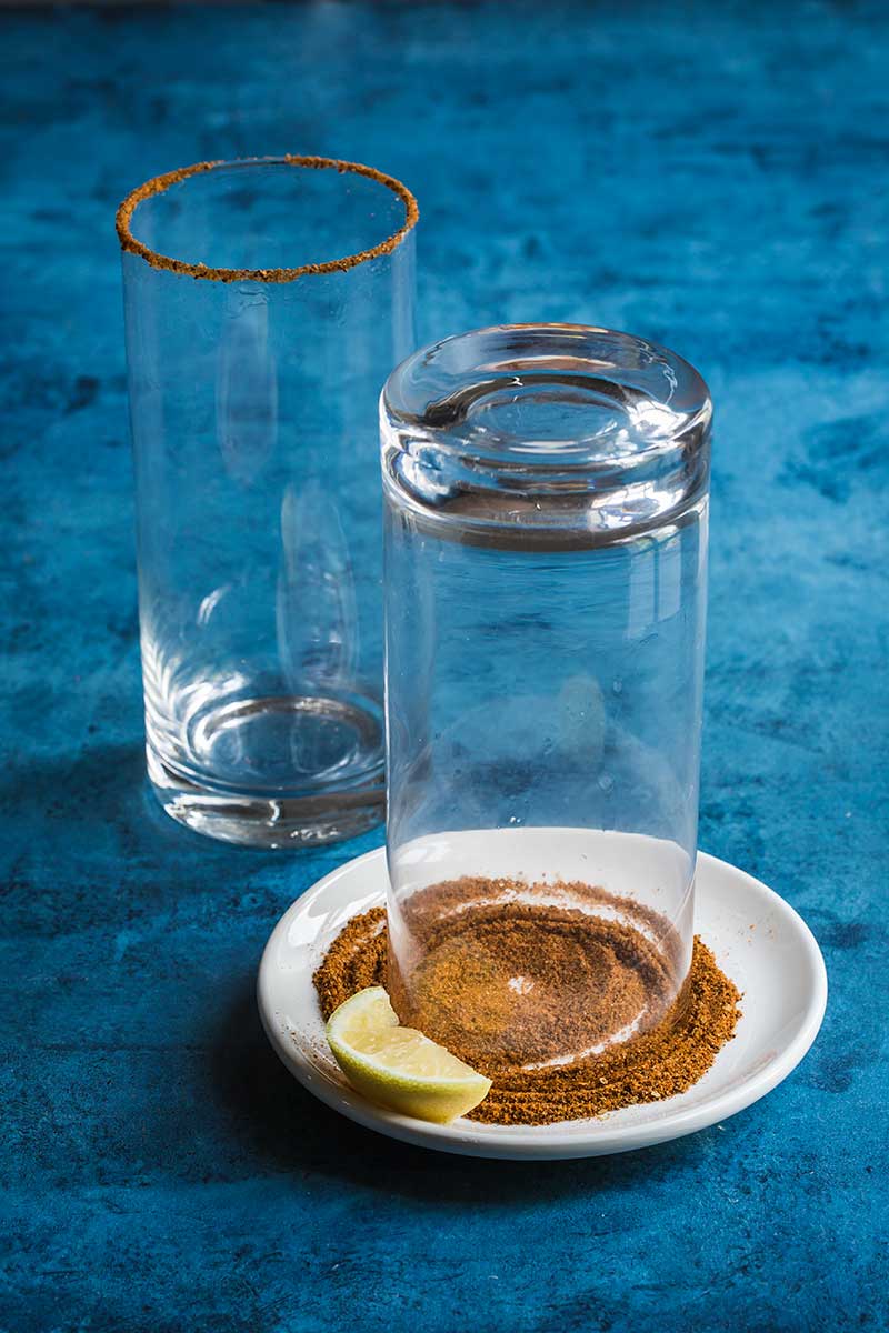 A highball glass turned over on a small plate covered with Old Bay Seasoning for the rim