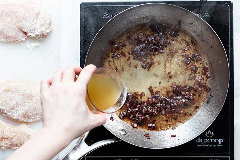 A hand pouring chicken stock into the skillet