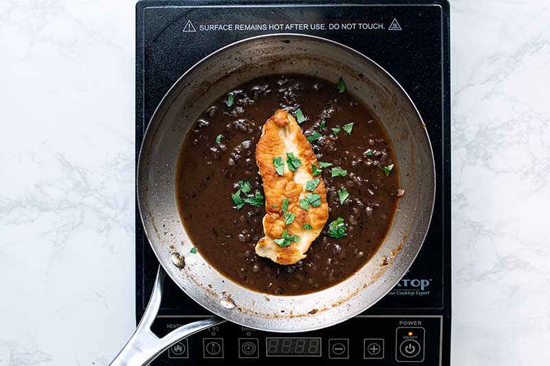 The cooked chicken placed back into the skillet over the pan sauce, topped with parsley