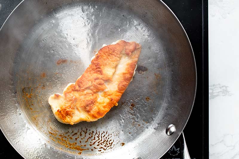 Crispy golden chicken in a stainless steel skillet after being flipped in the pan